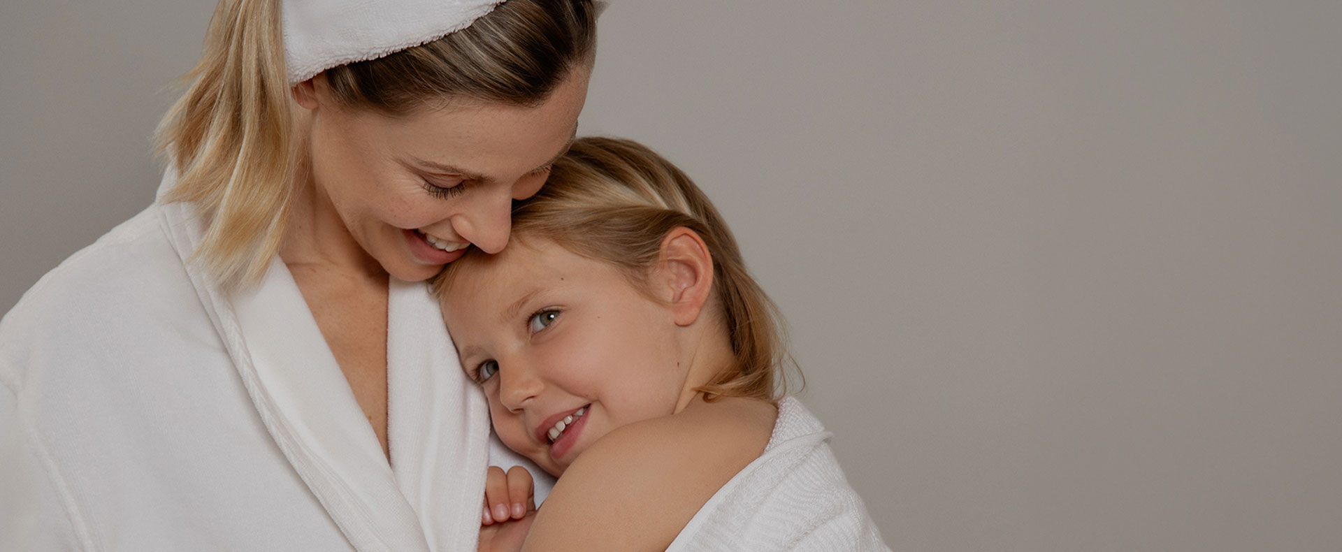 A mother cuddles lovingly with her child. Both wear soft VOSSEN bathrobes and enjoy a warm moment after bathing